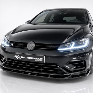 Front view of a glossy black car in a studio, with illuminated LED headlights and a VW emblem on the grille, Motordrome Design plate visible.