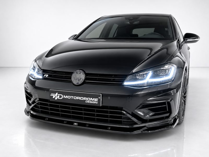 Front view of a glossy black car in a studio, with illuminated LED headlights and a VW emblem on the grille, Motordrome Design plate visible.