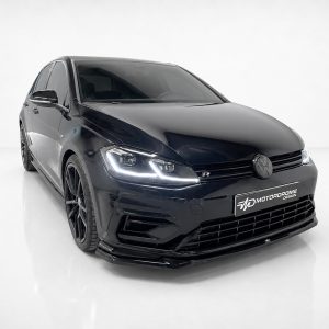 Front three-quarter view of a glossy black Volkswagen Golf R with a custom body kit and large black wheels in a white studio setting, logo plate visible on the bumper.