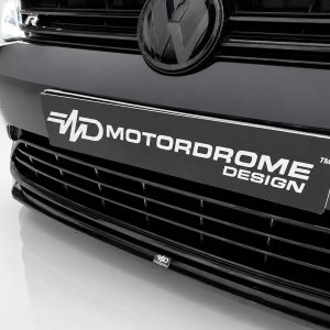 Close-up of a black VW car front with the VW emblem and a license plate reading 'Motordrome Design'.