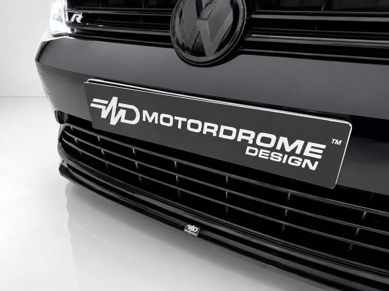 Close-up of a black VW car front with the VW emblem and a license plate reading 'Motordrome Design'.