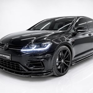 Black Volkswagen hatchback with glossy finish, large black alloy wheels, and bright LED headlights in a showroom setting.