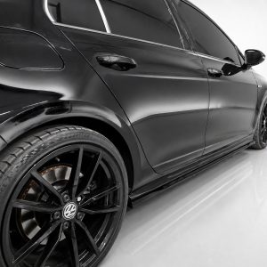 Close-up of a glossy black luxury sedan's rear-side panel and large black alloy wheel in a studio setting, with reflections on the body.
