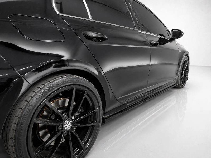 Close-up of a glossy black luxury sedan's rear-side panel and large black alloy wheel in a studio setting, with reflections on the body.