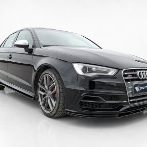 Black Audi S3 sedan in a studio, shown from a front three-quarter angle with large alloy wheels and glossy finish, showroom setting.