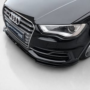 Front close-up of a glossy black Audi with the chrome grille, four-ring emblem, and sleek headlight visible.