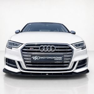 Front view of a white Audi sedan in a studio, showcasing its large chrome grille and four-ring emblem