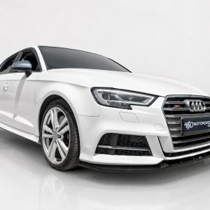 White Audi sedan shown from front-right in a bright studio, highlighting large alloy wheels and bold grille.