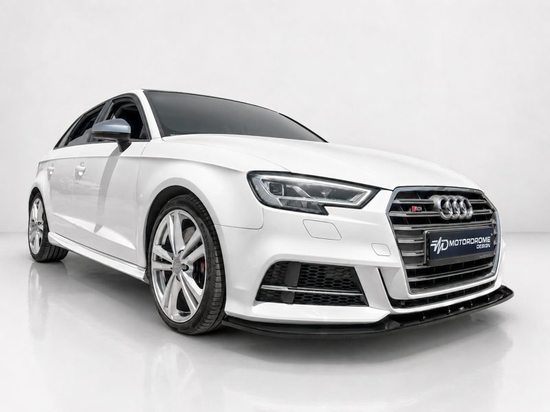 White Audi sedan shown from front-right in a bright studio, highlighting large alloy wheels and bold grille.