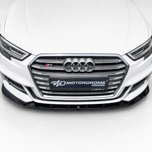 Front view of a white Audi with chrome grille and four-ring emblem, showing a Motordrome Design license plate