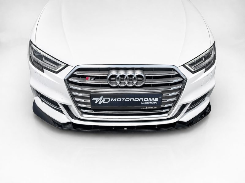 Front view of a white Audi with chrome grille and four-ring emblem, showing a Motordrome Design license plate