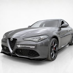 Gray Alfa Romeo sports car in a bright studio, front three-quarter view with a dealership plate reading 'MOTOR DROME DESIGN'.