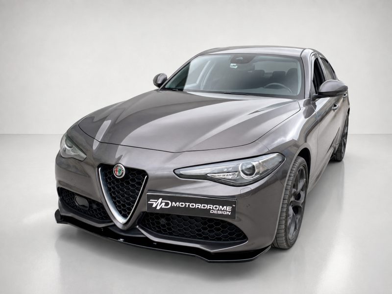 Front three-quarter view of a metallic gray Alfa Romeo sports sedan with a black honeycomb grille and a Motordrome Design plate in a studio setting