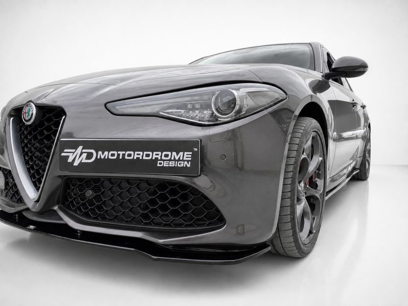 Front-left close-up of a gray Alfa Romeo sports car with a Motordrome Design plate on the bumper to the left.