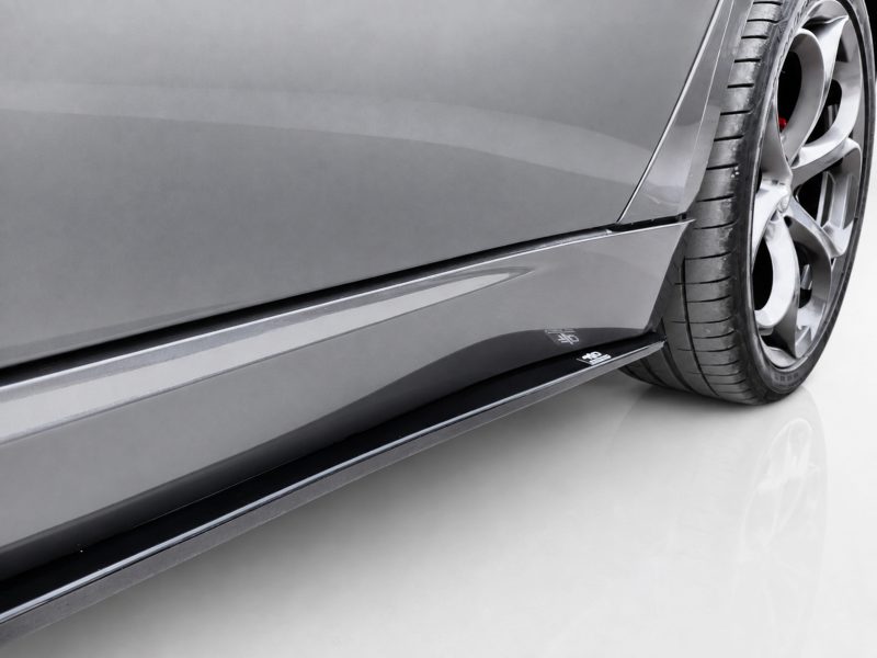 Close-up of a gray sports car's side panel, showing the lower body line and alloy wheel with tire.