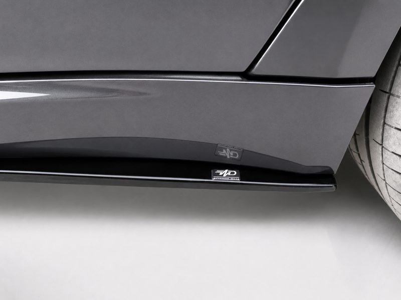 Close-up of a dark gray car's lower side panel with glossy trim and a small 'MD' branding badge near the wheel.