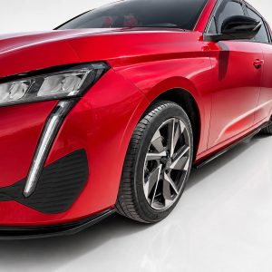 Close-up of a red modern sedan showing the front left headlight, fender, and alloy wheel on a white studio backdrop.