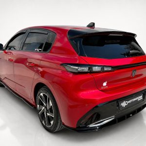 Rear three-quarter view of a glossy red hatchback with black rear window, distinctive taillights, and large multi-spoke wheels in a white studio setting