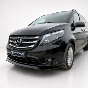 Black Mercedes minivan in a studio setting, angled front view showing grille and headlights with a Motordrome license plate tag on the bumper.