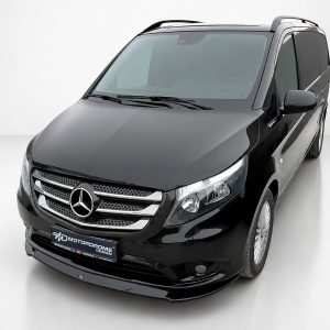 Front-left angled view of a glossy black Mercedes-Benz van, showing the grille, emblem and headlights in a studio setting.