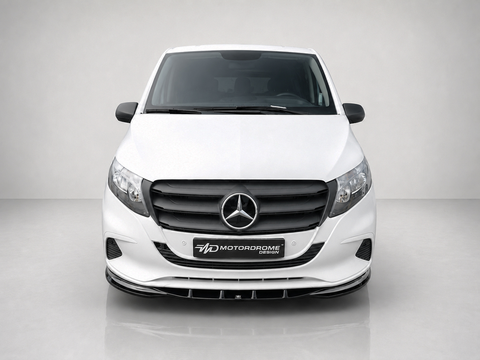 K190-002_1jpg - OPSHOLDERS Front view of a white Mercedes van with black grille and prominent Mercedes emblem, headlights on each side, and a dealer plate reading 'MOTOR DROME DESIGN'