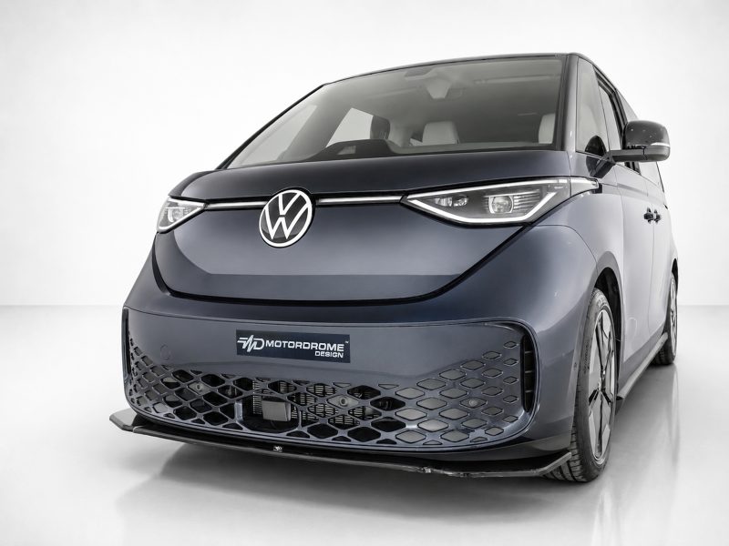 Front-left angled view of a dark blue Volkswagen minivan concept with prominent VW emblem and honeycomb lower grille; showroom backdrop shows 'Motordrome Design' plate.