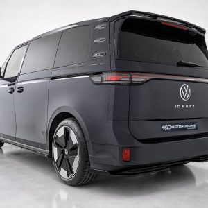 Rear three-quarter view of a dark VW ID. Buzz concept van in a studio, showing the VW logo and slim taillights with a red light strip.