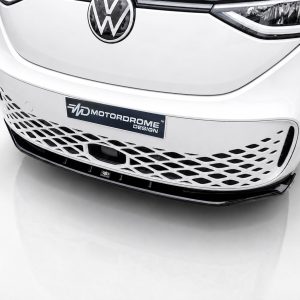 Front view of a white car’s grille with a Volkswagen emblem and a mesh lower grille reading 'MOTORDROME DESIGN' on a dark plate