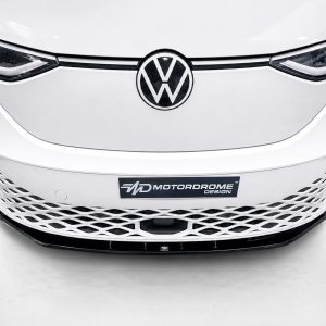 Front view of a white Volkswagen car highlighting the VW emblem and a lattice-style lower grille with a MotorDrome Design plate beneath it