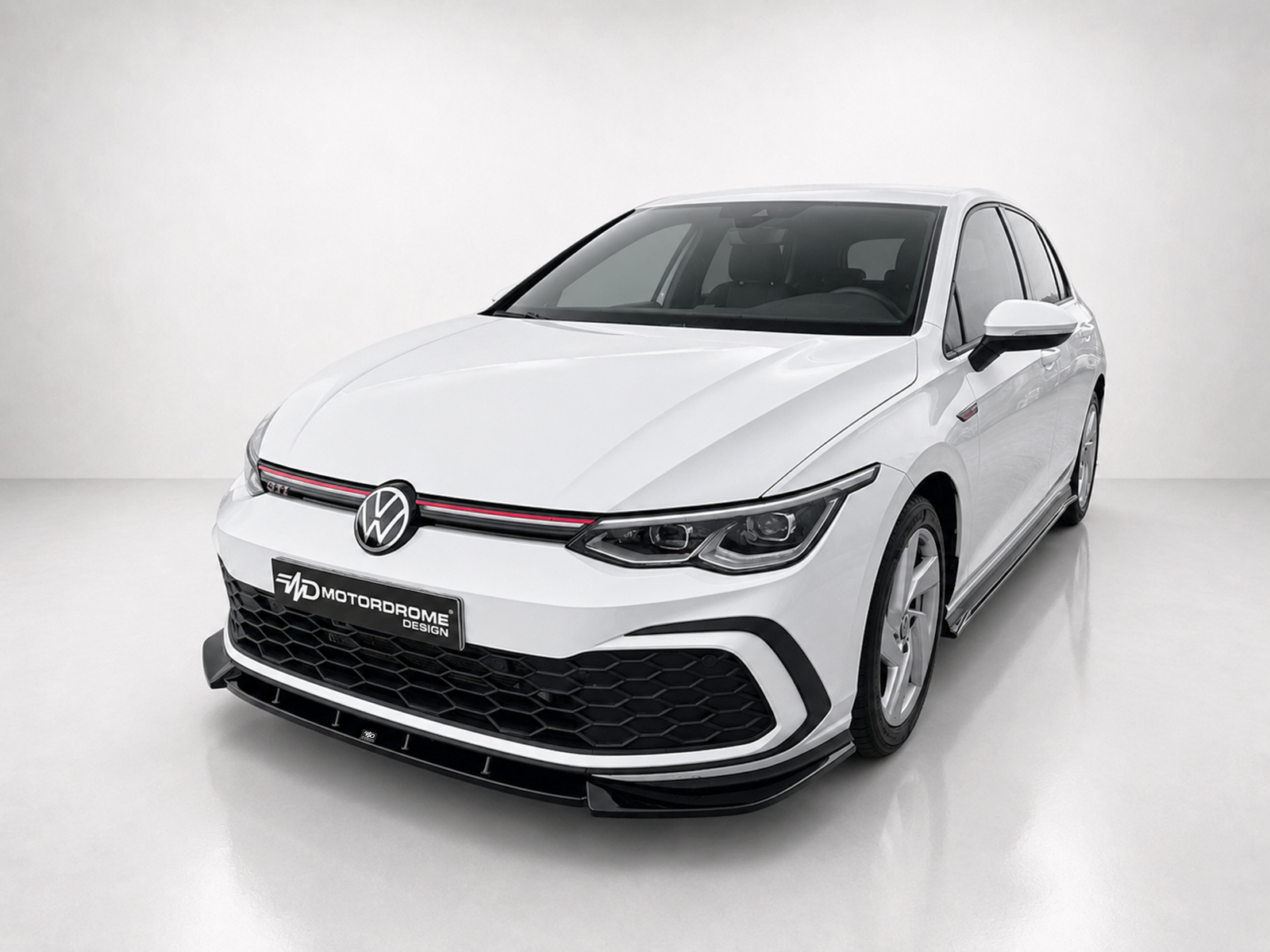 K192-001_2jpg - OPSHOLDERS Front three-quarter view of a white Volkswagen car in a studio setting, showing the VW emblem, black honeycomb grille, and red accent stripe along the grille.