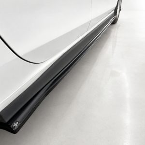 K192-002_4jpg - OPSHOLDERS Close-up of a white car's side with a black running board and a small logo at the bottom edge.