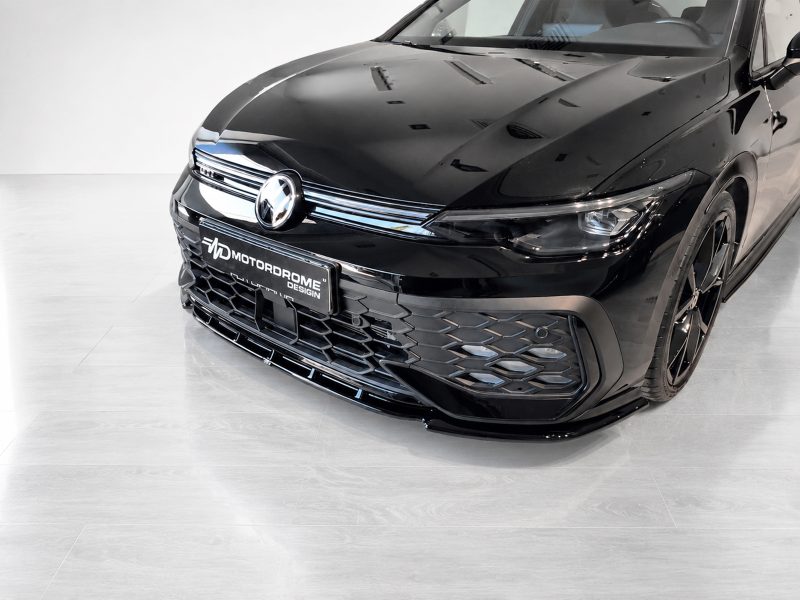 Front of a glossy black car in a showroom, with a chrome grille and a Motordrome Design license plate.