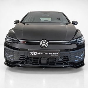 Front view of a black Volkswagen Golf GTI in a studio, showing the VW emblem and honeycomb grille with GTI badge on the side.