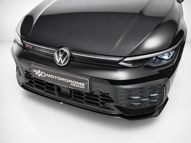 Front view of a glossy black Volkswagen with GTI badge and illuminated headlights on the right side.