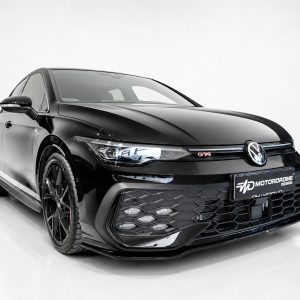 Front-left three-quarter view of a glossy black Volkswagen with a honeycomb grille and red GTI badge in a studio setting.