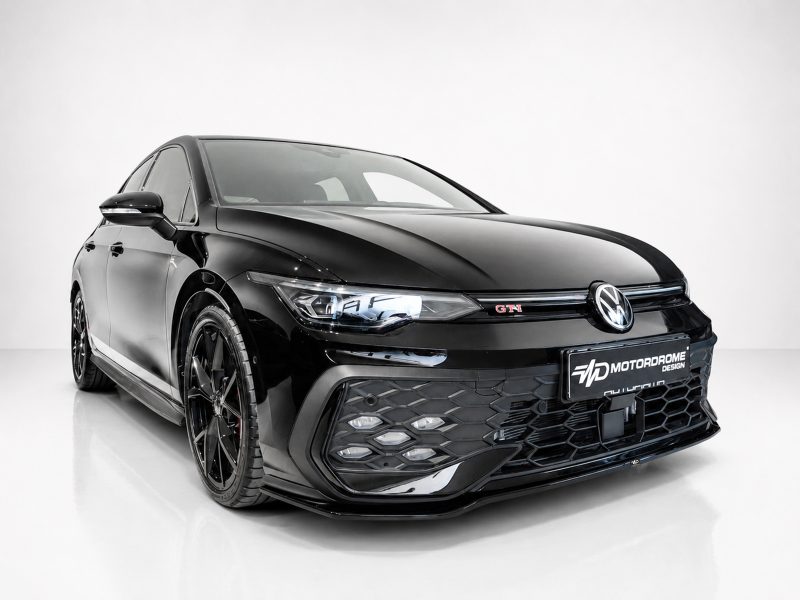 Front-left three-quarter view of a glossy black Volkswagen with a honeycomb grille and red GTI badge in a studio setting.