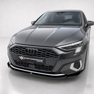 Front three-quarter view of a dark gray Audi sedan with a hexagonal grille and LED headlights in a bright studio setting