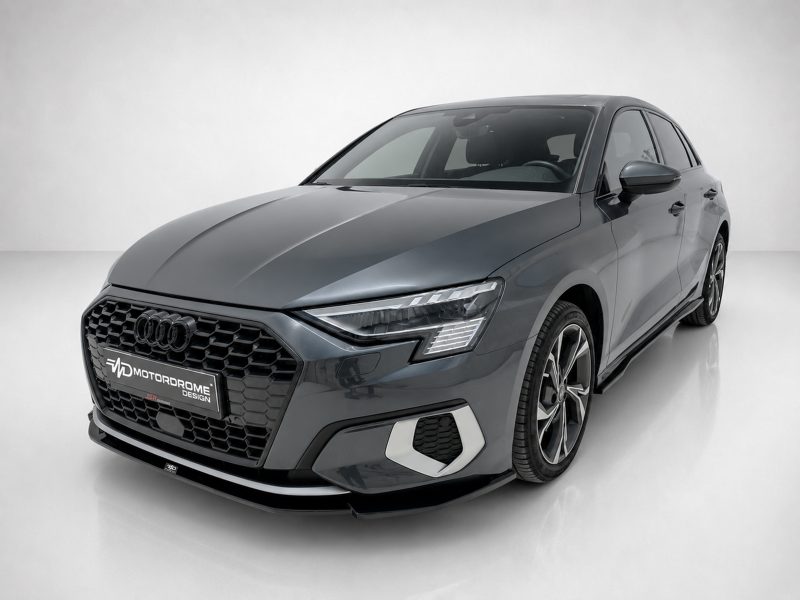 Front three-quarter view of a gray Audi sedan in a studio setting, highlighting the hexagonal grille and LED headlights.