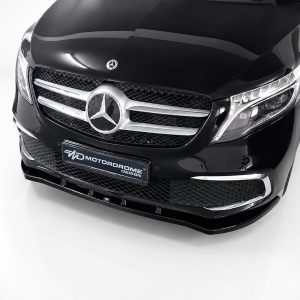 Front view of a black Mercedes-Benz with prominent chrome grille and emblem in a showroom setting, low angle perspective, license plate visible reading MOTORDROME DESIGN