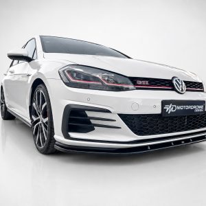 White Volkswagen GTI in a three-quarter front view in a studio setting, showing the honeycomb grille and red trim detail