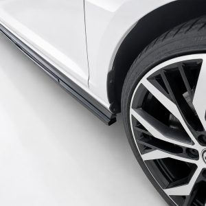 Close-up of a white car's side with a chrome rocker trim and a large black-and-silver alloy wheel visible at the front-right edge, tire labeled outside edge.