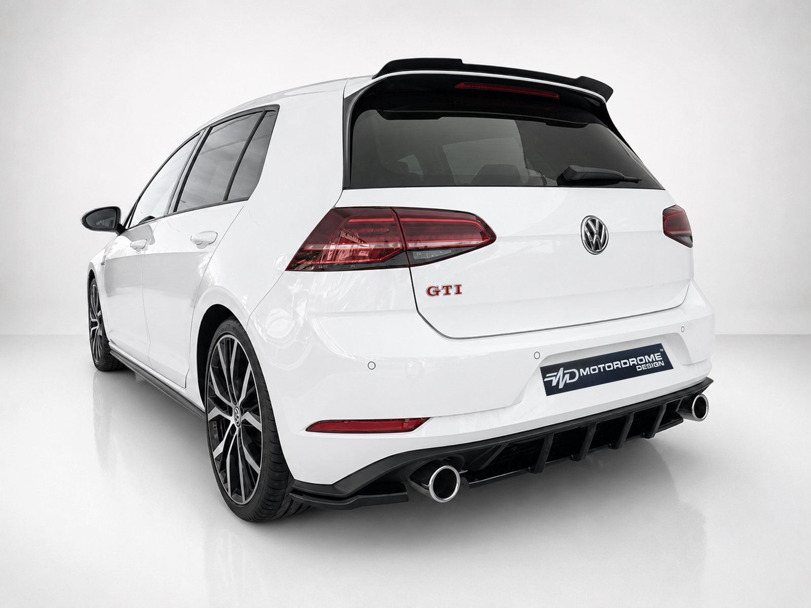 K196-004_2jpg - OPSHOLDERS Rear three-quarter view of a white VW Golf GTI wagon with a large black diffuser and dual exhausts on a white studio backdrop, Motordrome Design plate visible.