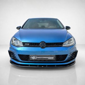 Front view of a metallic blue Volkswagen GTI in a studio with a honeycomb grille and Motordrome Design plate on the bumper.