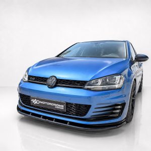 Blue Volkswagen GTI-style car shown in a three-quarter front view in a studio, with a black honeycomb grille and Motordrome Design plate on the bumper.