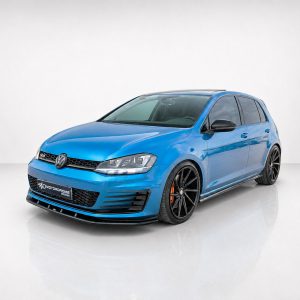 Front three-quarter view of a bright blue modified VW hatchback with black alloy wheels in a studio setting.