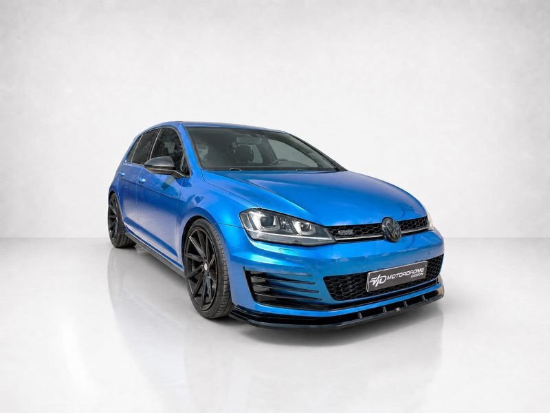 Blue Volkswagen hatchback viewed from the front-right in a studio setting, showcasing a black front lip and large black alloy wheels (aftermarket styling).