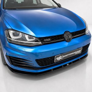 Front three-quarter view of a blue Volkswagen GTI in a studio, showing the grille, headlights, and badge against a white backdrop.