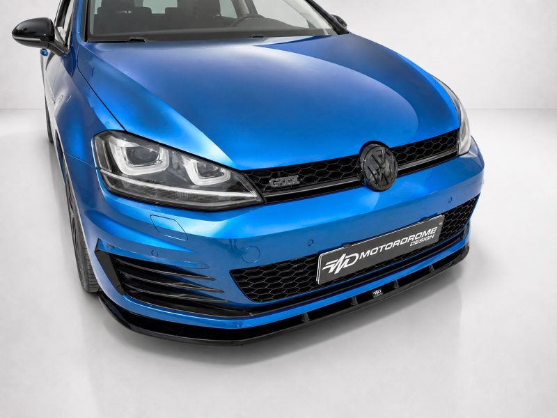Front three-quarter view of a blue Volkswagen GTI in a studio, showing the grille, headlights, and badge against a white backdrop.