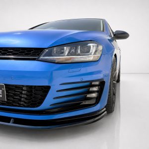 Front-left view of a bright blue Volkswagen with headlight, grille, and lower diffuser visible in a studio setting, license plate partially shown in the corner