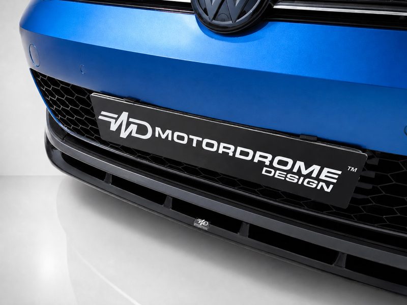 Close-up of a blue car front featuring a black license plate reading MOTORDROME DESIGN and a honeycomb grille below.